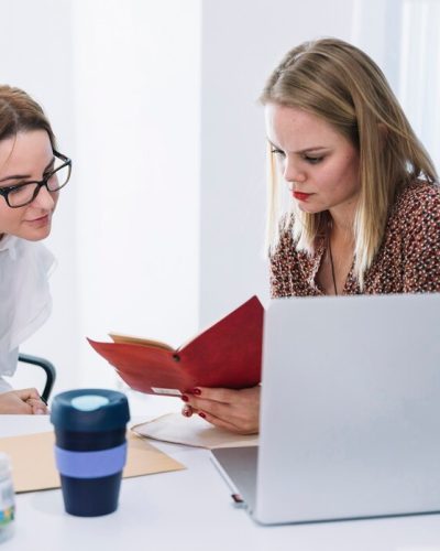 two-female-businesspeople-reading-diary-office_23-2147955052